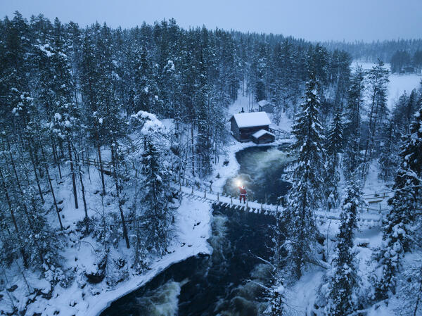 Santa Claus with lantern on the suspended bridge above the frozen rapids, Myllykoski, Juuma, Oulanka National Park, Kuusamo, Lapland, Finland (MR)