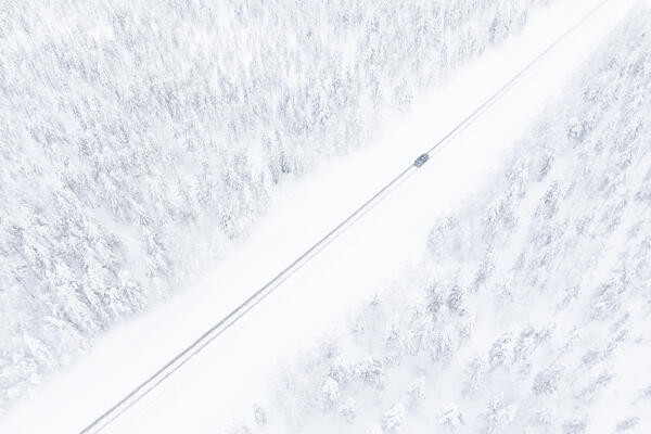 aerial view of a car driving on the snowy road along the forests of lapland, Finland, Europe