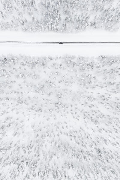 aerial view of a car driving on the snowy road along the forests of lapland, Finland, Europe
