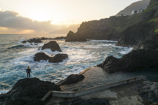 a man enjoys the warm light of the sunrise at the natural pools of Seixal, Madeira, Portugal, Europe