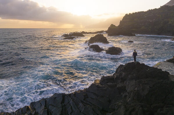 a man enjoys the warm light of the sunrise at the natural pools of Seixal, Madeira, Portugal, Europe