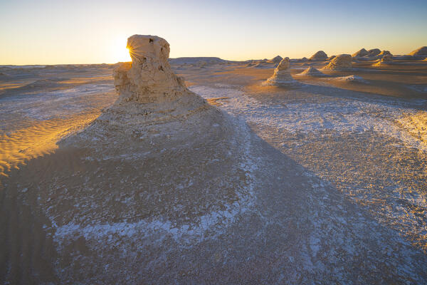 The first rays of the sun illuminate the spectacular rock formations of the incredible landscape of the White Desert, during a beautiful winter day, Egypt, Africa