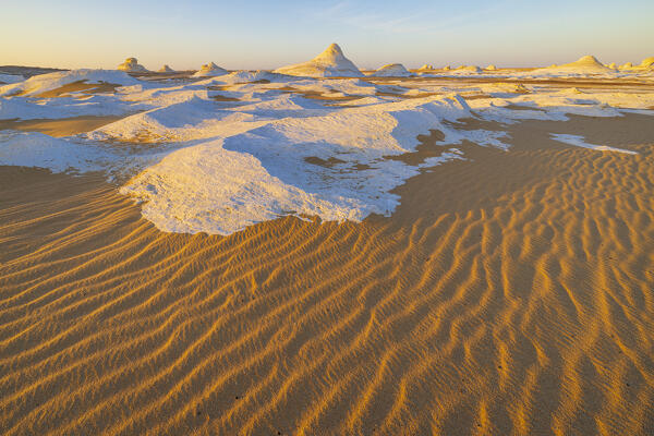 The first rays of the sun illuminate the spectacular rock formations of the incredible landscape of the White Desert, during a beautiful winter day, Egypt, Africa