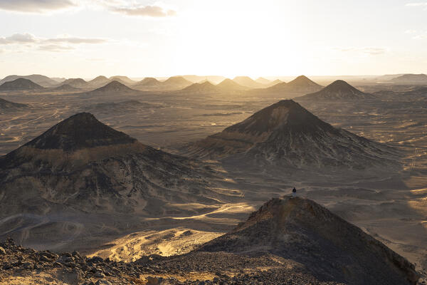 a boy admires the beautiful sunset from the old volcano in to Black Desert, Egypt, Africa