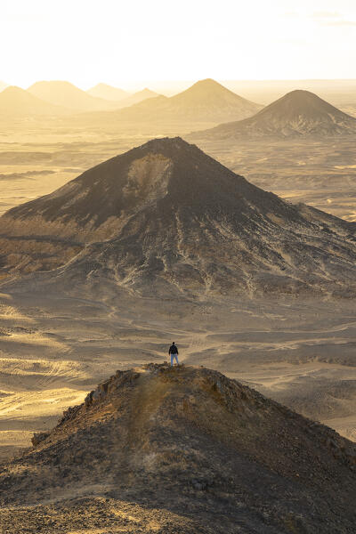 a boy admires the beautiful sunset from the old volcano in to Black Desert, Egypt, Africa