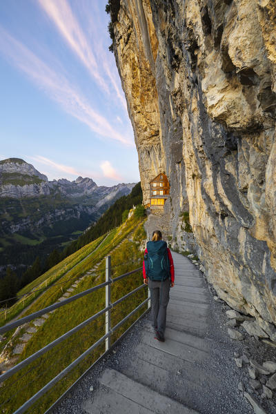 A woman walks to Äescher, Berggasthaus at sunrise during summer, Wasserauen, Ebenalp, Canton Appenzell Innerrhoden, Alpstein, Schwende, Switzerland, Western Europe (MR)