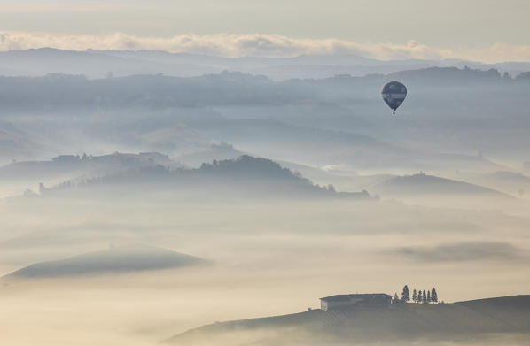 An hot air balloon flies over vineyards and mist during autumn, Cuneo, Langhe e Roero, Piedmont, Italy, Southern Europe