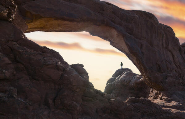 A man stands in a natural Arch at sunset, Arches National Park, Moab, Utah, North America, USA