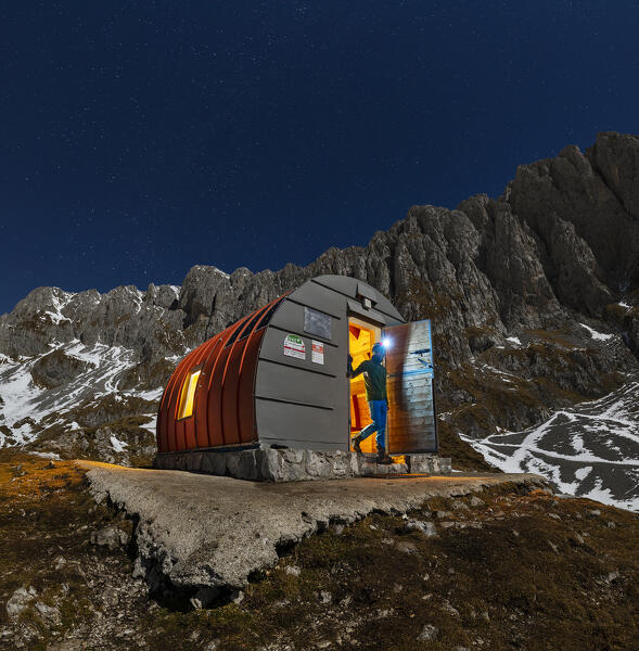 A trekker comes out of illuminated Città di Clusone Bivouac during night, Castione della Pesolana, Prealpi Orobie, Bergamo, Lombardy, Italy, Southern Europe (MR)