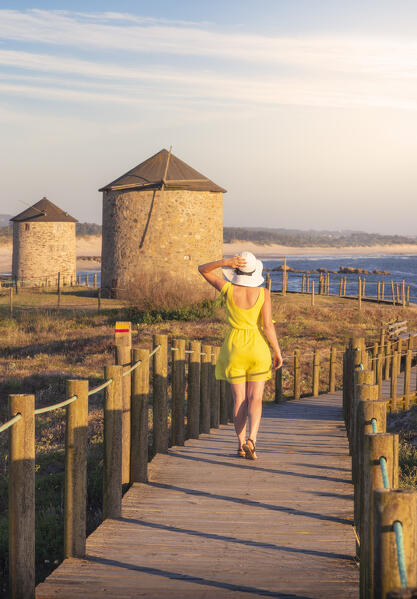 A tourist walks over wooden walkay around Apulia Windmills at sunset, Apulia, Esposende, Braga, Norte, Portugal, Iberian Peninsula, Western Europe
