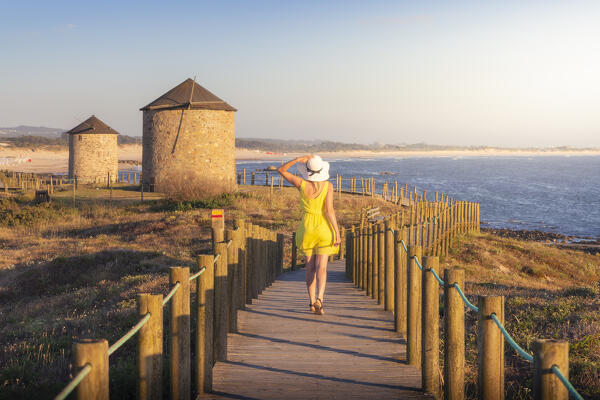 A tourist walks over wooden walkay around Apulia Windmills at sunset, Apulia, Esposende, Braga, Norte, Portugal, Iberian Peninsula, Western Europe (MR)