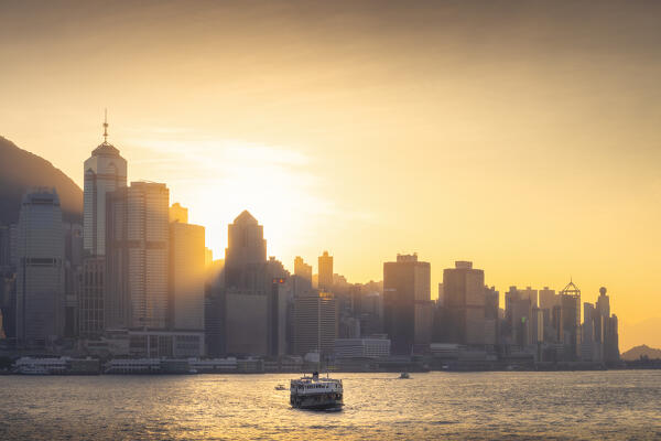 A boat sails in front of cityscape of Hong Kong during sunset, Tsim Sha Tsui, Kowloon, Hong Kong, China, Asia
