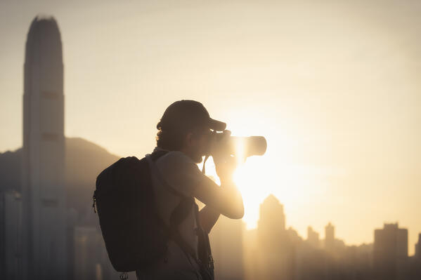 A tourist takes a picture of cityscape during sunset viewed from Avenue of Stars, Tsim Sha Tsui, Kowloon, Hong Kong, China, Asia