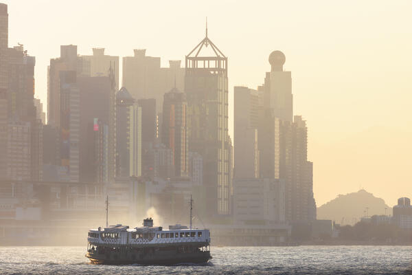 A boat sails in front of cityscape of Hong Kong during sunset, Tsim Sha Tsui Kowloon, Hong Kong, China, Asia
