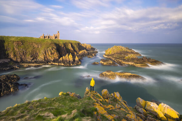 A tpurist observes Slains Castle at sunset, Cruden Bay, Aberdeenshire, Scotland, United Kingdom