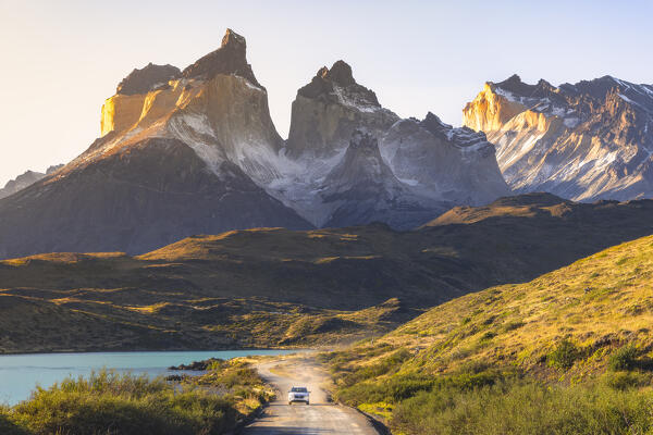 A car travels along the Torres del Paine NP unpaved road with Cuernos del Paine in the background during sunset, Ultima Esperanza, Region de Magallanes y de la Antartica Chilena, Patagonia, Chile, South America