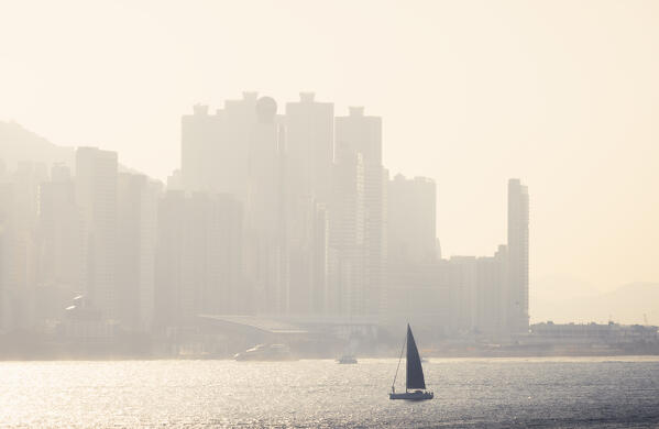 A boat sails in front of cityscape of Hong Kong during sunset, Tsim Sha Tsui, Kowloon, Hong Kong, China, Asia