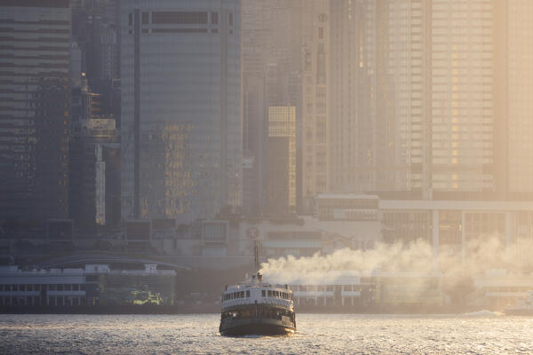 A boat sails in front of cityscape of Hong Kong during sunset, Tsim Sha Tsui, Kowloon, Hong Kong, China, Asia