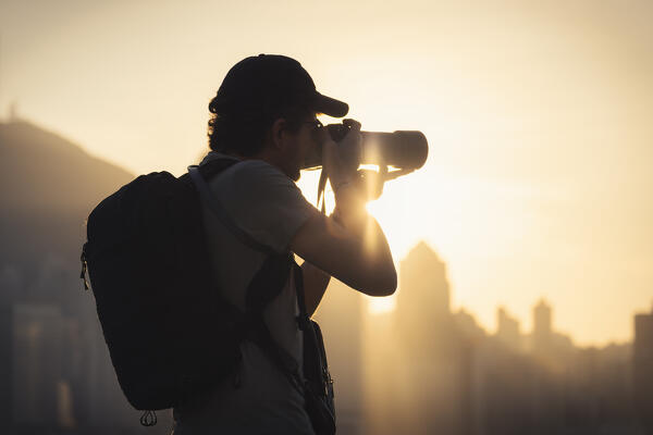 A tourist takes a picture of cityscape during sunset viewed from Avenue of Stars, Tsim Sha Tsui, Kowloon, Hong Kong, China, Asia