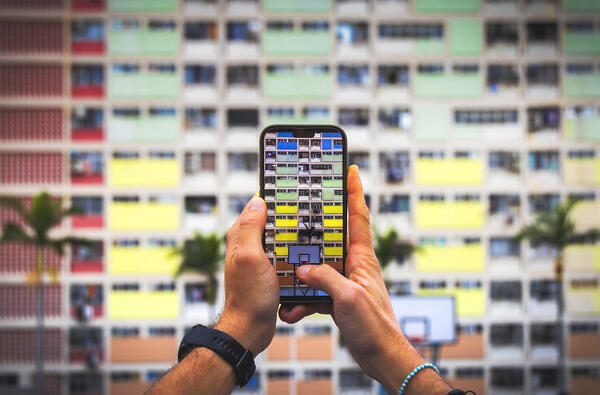 A tourist takes a picture with his phone of Choi Hung Estate rooftop basketball court and rainbow buildings, Ngau Chi Wan, Kowloon, Hong Kong, China, Asia