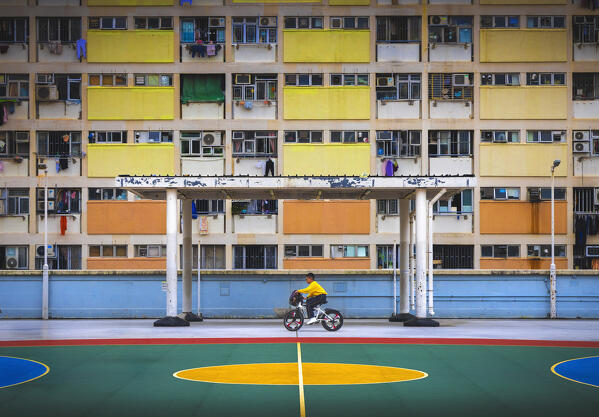 A child pedals his bike at Choi Hung Estate rooftop basketball court and rainbow buildings, Ngau Chi Wan, Kowloon, Hong Kong, China, Asia