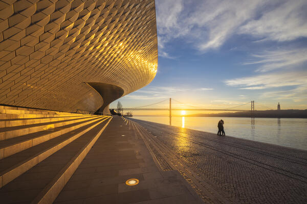 A couple kiss during sunrise at Maat Museum with 25 April Bridge in the background, Belem, Lisbon, Portugal, Iberian peninsula, Western Europe