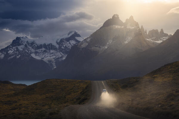 A car travels along the Torres del Paine NP unpaved road with Mountains in the background during sunset, Ultima Esperanza, Region de Magallanes y de la Antartica Chilena, Patagonia, Chile, South America