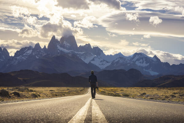 A tourist walks on the main road to el Chalten with Fitz Roy in the background during sunset, El Chalten, Parque Nacional Los Glaciares, Santa Cruz, Patagonia Argentina, Argentina, South America