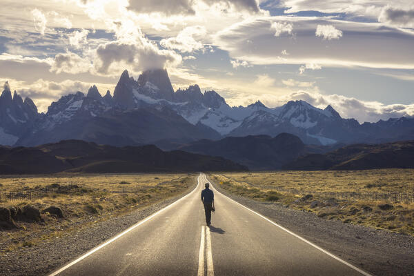 A tourist walks on the main road to el Chalten with Fitz Roy in the background during sunset, El Chalten, Parque Nacional Los Glaciares, Santa Cruz, Patagonia Argentina, Argentina, South America
