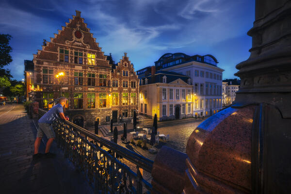 A tourist observes illuminated Guil Houses from St. Michael’s Bridge during night, Gand, Belgium, East Flanders, Flanders, Western Europe
