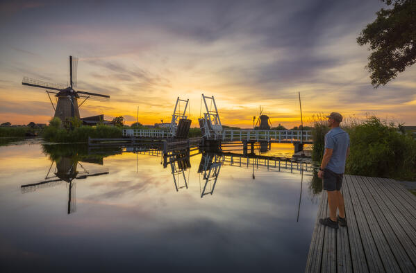 A tourist observes a windmill in Kinderdijk during sunset in summer, Molenlanden, Netherlands, South Holland, Western Europe