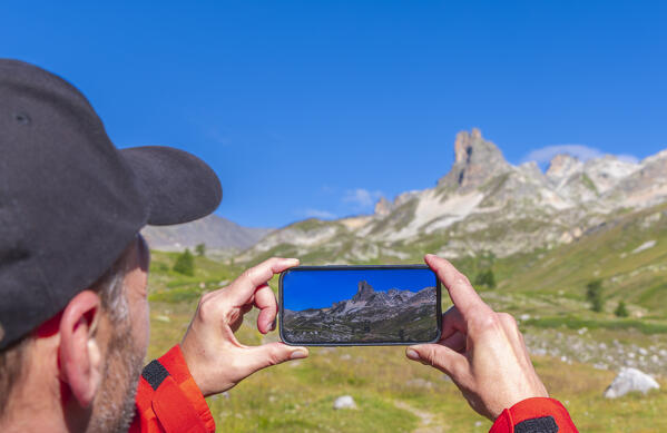 A hiker photographs Le Grand Adret at sunrise during summer, Provence Alps Cote d’Azur, Haute Alps, Vallee Etroite, France, Europe