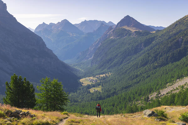 A hiker observes Les Granges de la Vallee Etroite from an elevated point of view in front of Chaberton group, Provence Alps Cote d’Azur, Haute Alps, Vallee Etroite, France, Europe