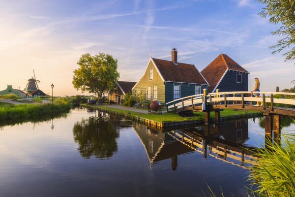 A tourist walks on a bridge in front of a typical house in Zaanse Schans during sunset in summer, Zaandam, Zaanstad, Netherlands, North Holland, Western Europe