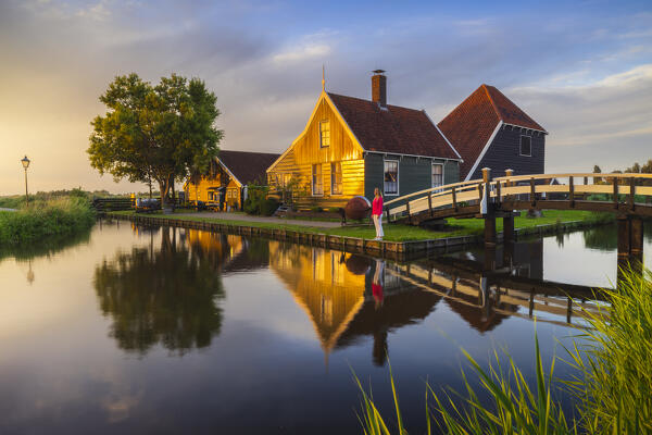 A tourist observes sunset in front of a typical house in Zaanse Schans during summer, Zaandam, Zaanstad, Netherlands, North Holland, Western Europe