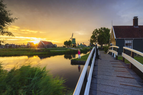 A tourist observes sunset in front of a typical house in Zaanse Schans during summer, Zaandam, Zaanstad, Netherlands, North Holland, Western Europe