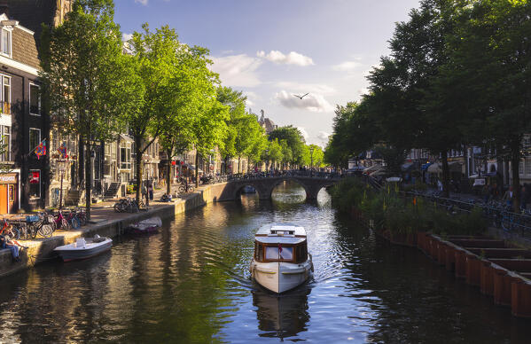A boat along canals in Amsterdam at sunset during summer, Oudezijds Voorburgwal, De Wallen, Binnenstad, Netherlands, North Holland, Western Europe
