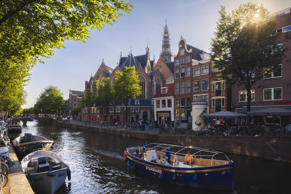 A boat along canals in front of Oude Kerk in Amsterdam at sunset during summer, Oudezijds Voorburgwal, De Wallen, Binnenstad, Netherlands, North Holland, Western Europe