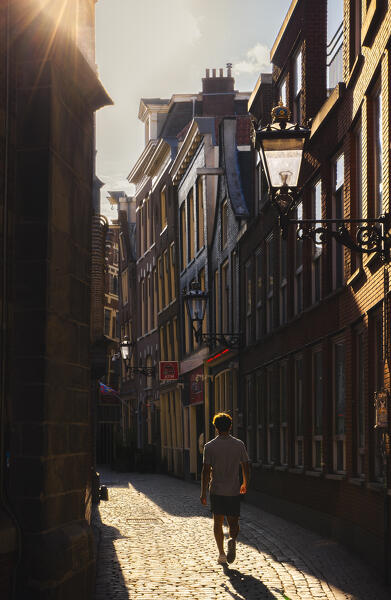 A tourist walks in an alley of Amsterdam during sunset in summer, De Wallen, Binnenstad, Netherlands, North Holland, Western Europe