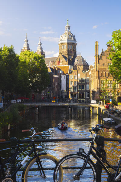 A boat along canals in front of Basilica of St Nicholas in Amsterdam at sunset during summer, Oudezijds Voorburgwal, De Wallen, Binnenstad, Netherlands, North Holland, Western Europe