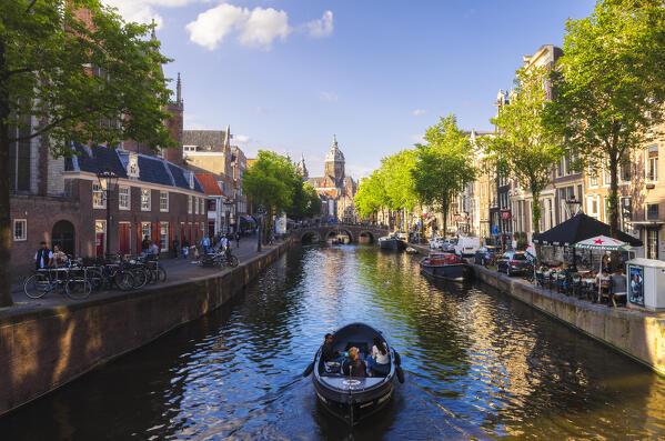 A boat along canals with Basilica of St Nicholas in the background during sunset, Amsterdam, Oudezijds Voorburgwal, De Wallen, Binnenstad, Netherlands, North Holland, Western Europe