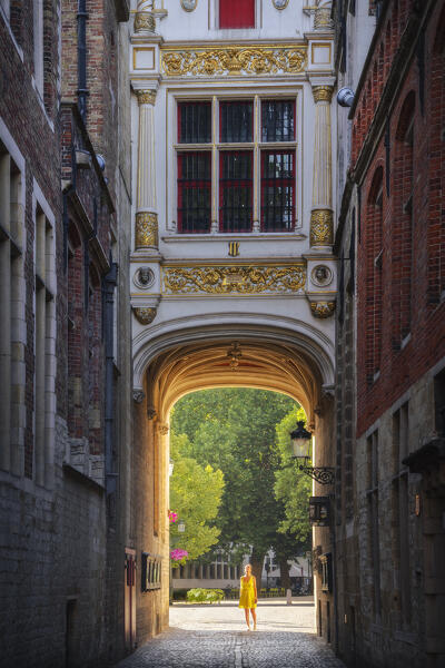A tourist walks under arch of the Liberty of Bruges during sunset, Belgium, West Flanders, Flanders, Western Europe (MR)