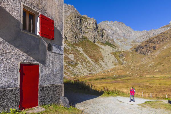 A trekker walks towards the shelter Pian del Re surrounded by mountains, Pian del Re, Crissolo, Cuneo, Piedmont, Italy, Southern Europe
