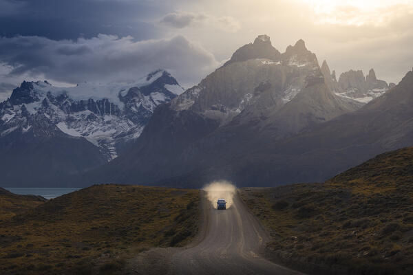 A car travels along the Torres del Paine NP unpaved road with Mountains in the background during sunset, Ultima Esperanza, Region de Magallanes y de la Antartica Chilena, Patagonia, Chile, South America