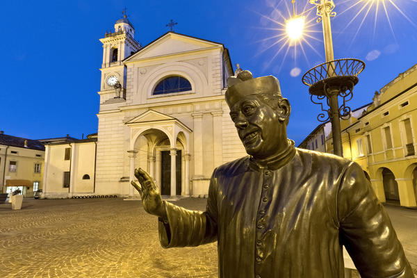 Brescello: the statue of Don Camillo and the Santa Maria Nascente church. The village is famous for the films of Don Camillo and Peppone inspired by the books of Giovannino Guareschi. Reggio Emilia province, Emilia Romagna, Italy, Europe.