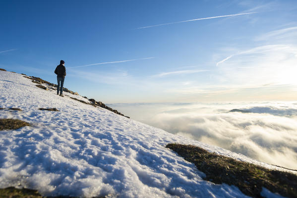 Monte Galbiga, Como province, Lombardy, Italy, Europe. Girl standing in the snow and looking at a sea of clouds