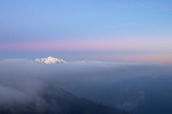 Alpe di Lenno, Como province, Lombardy, Italy, Europe. Grigna's snowy peak emerging from a sea of clouds after sunset 