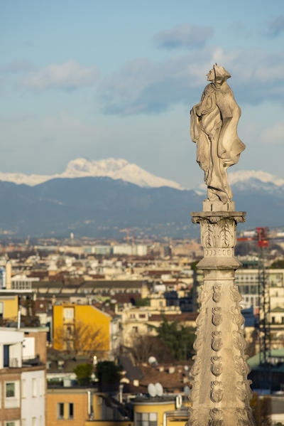 Milan, Lombardy, Italy, Europe. A statue on the top of a spier on the rooftop of Milano Cathedral, city and prealps in the background