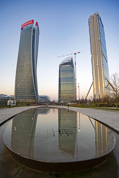 Milano, Lombardy, Italy, Europe. The three towers of CityLife reflect in the water of a fountain at dusk