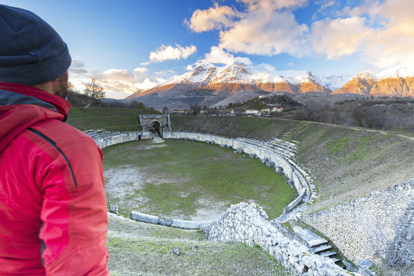 Man admires the sunset from the amphitheatre of the roman archeological site of Alba Fucens with majestic Apennines mountain of Sirente Velino regional park, Marsica district, L’Aquila province, Abruzzo, Italy